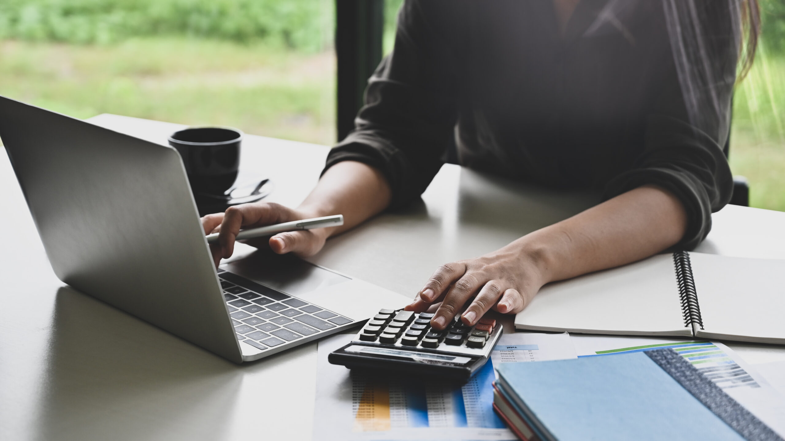 Closeup of a woman working with finance data on calculator and laptop.