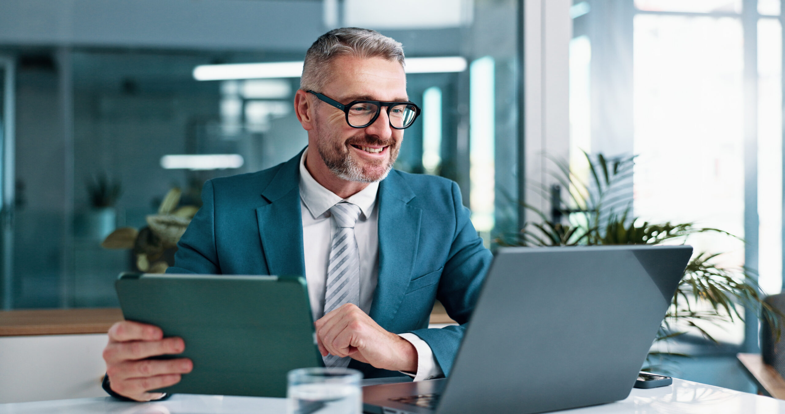 businessman sitting at a desk with a tablet and a laptop